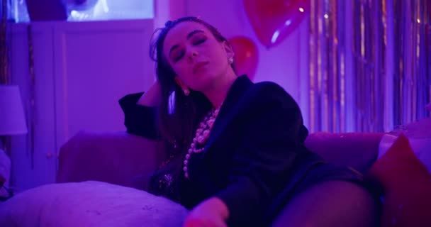 Приваблива молода жінка розслабляється на дивані в освітленому будинку під час вечірки в Галентінах - Кадри, відео