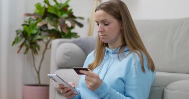 Gericht vrouw in blauwe hoodie met behulp van smartphone en creditcard voor online aankopen thuis. Hoge kwaliteit 4k beeldmateriaal - Video