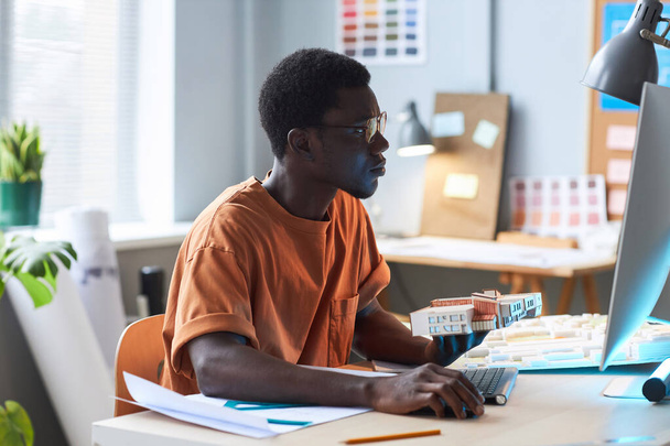Arquitecto joven afroamericano sentado en su lugar de trabajo y trabajando en la computadora en la oficina - Foto, imagen