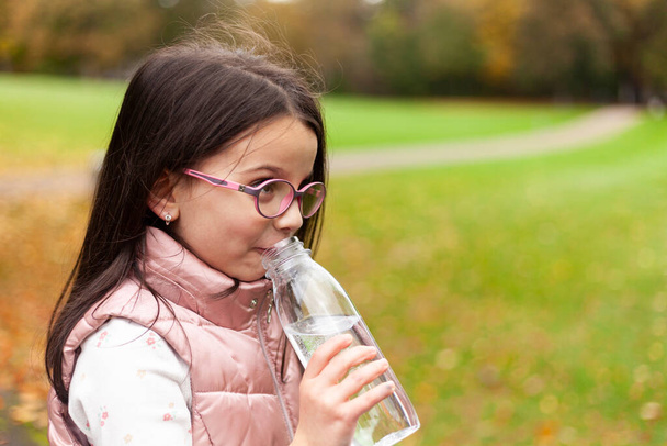 Carina bambina che beve acqua da una bottiglia nel parco autunnale - Foto, immagini