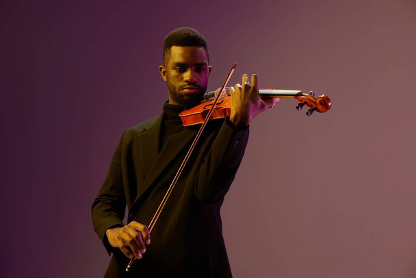 Elegante hombre de traje tocando el violín sobre un vibrante fondo púrpura, creando una interpretación musical armoniosa y fascinante - Foto, Imagen