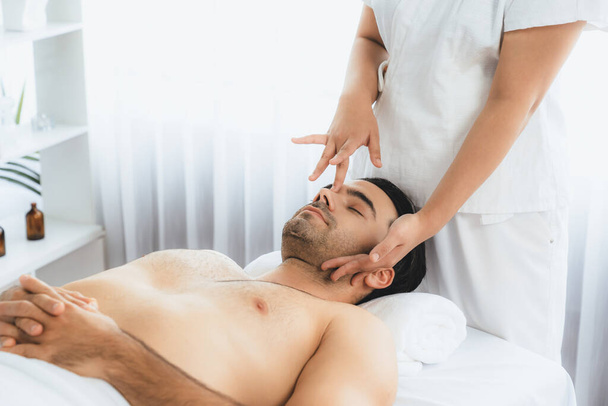 Homme caucasien appréciant relaxant massage de la tête anti-stress et dorloter beauté faciale loisirs de la peau dans dayspa lumière moderne ambiant au complexe de luxe ou salon de spa de l'hôtel. Tranquillité - Photo, image