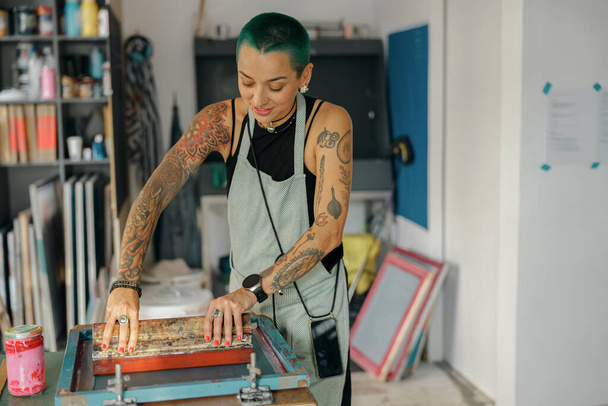 Trabalhadora feminina com rodo está pressionando tinta no quadro trabalhando no estúdio de design. Serigrafia - Foto, Imagem