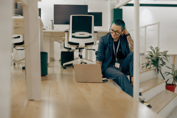 Kreative tätowierte Geschäftsfrau mit grünen kurzen Haaren arbeitet im modernen Büro am Laptop - Foto, Bild
