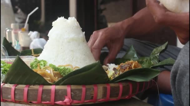 Los hombres comen arroz tumpeng (arroz con cono) servido con urap-urap (ensalada indonesia), pollo frito y fideos. El arroz Tumpeng generalmente se sirve para el día de acción de gracias. - Metraje, vídeo