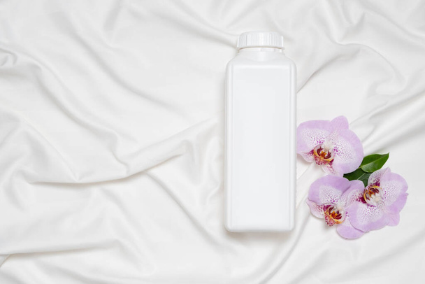 Détergent à lessive liquide ou adoucissant pour tissus sur literie, fleurs d'orchidée, vue de dessus. - Photo, image