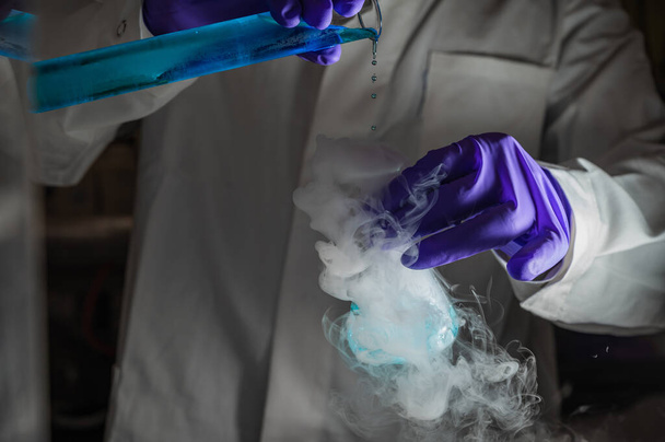 Дымные эксперименты с голубыми капельками. Ученый работает над химической реакцией, генерируя густой дым из стеклянной колбы. Copyspace - Фото, изображение
