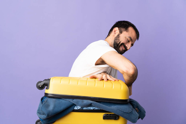 Traveler caucasian man with a suitcase full of clothes over isolated purple background - Photo, Image