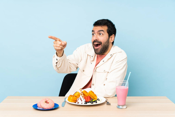 Человек за столом, завтракающий вафлями и молочный коктейль, указывающий в сторону - Фото, изображение