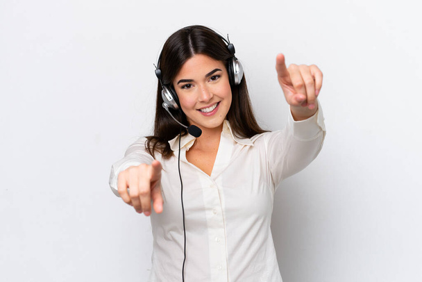 Telemarketer mujer caucásica trabajando con un auricular aislado sobre fondo blanco señala el dedo a usted mientras sonríe - Foto, imagen