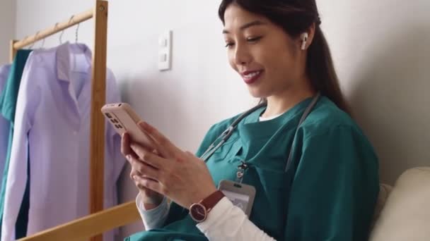 Nuoren iloisen sairaanhoitajan kallistaminen lääketieteellisessä univormussa tekstiviestissä älypuhelimella klinikalla - Materiaali, video