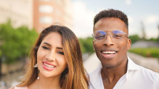 Pareja multiétnica de una mujer latina y un hombre africano mirando a la cámara y sonriendo al aire libre - Foto, imagen