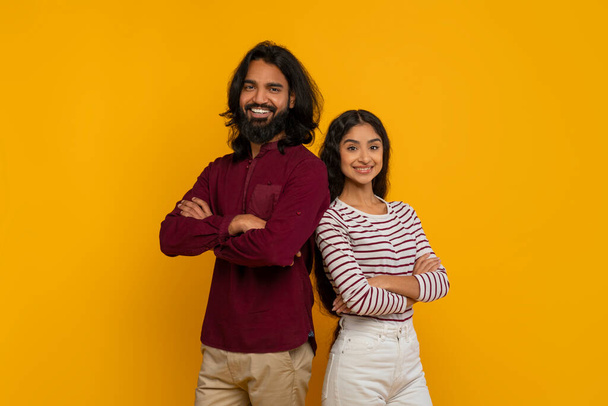 ポジティブな魅力的な若いインド人男性と女性は,黄色のスタジオの背景に隔離されたカメラで笑顔で胸に戻って背中をポーズ. チームワーク,友情コンセプト - 写真・画像