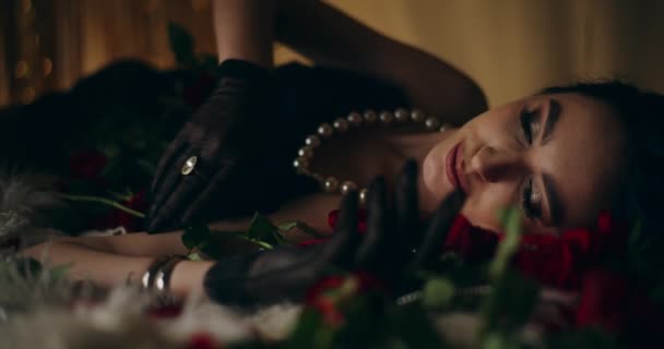 Primer plano de sensual mujer joven atractiva en collar de perlas acostado por rosas en la cama - Metraje, vídeo
