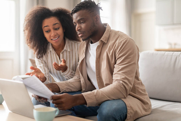 Páros pénzügyek. Fiatal afro-amerikai házastársak, nő és férfi, papírmunka mellett ül laptop számlázási és kínál leveleket, tervezési költségek együtt ül otthon - Fotó, kép