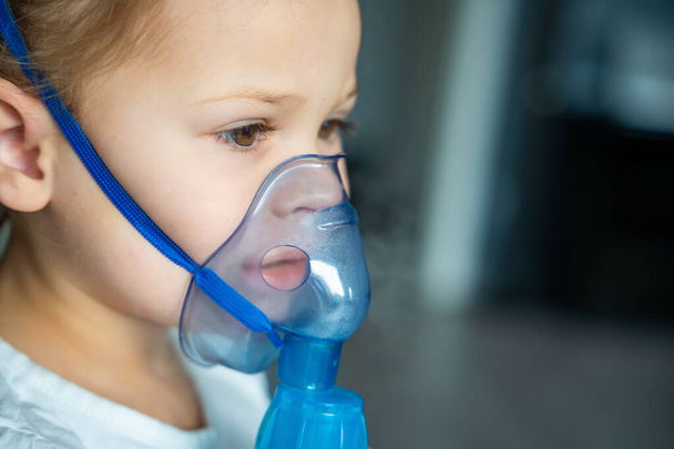 Söpö pikkutyttö istuu ja pitää nebulizer naamio nojaa kasvot, hengitysteiden hoito käsite. Laadukas kuva - Valokuva, kuva