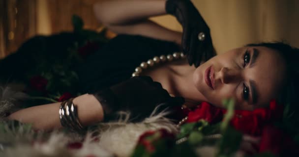 Sensual mujer joven en collar de perlas acostado por rosas en la cama - Metraje, vídeo