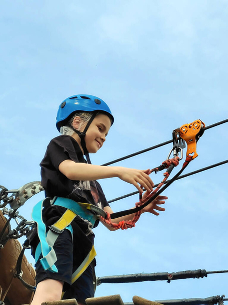 Un adolescent marche sur un pont suspendu de corde dans un parc d'attractions de corde. Vue d'en bas. Loisirs sportifs pour jeunes actifs - Photo, image