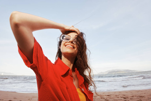 Lächelnde Frau mit Sonnenbrille, Freiheit umarmen, bunten Sonnenuntergang am Strand genießen - Foto, Bild