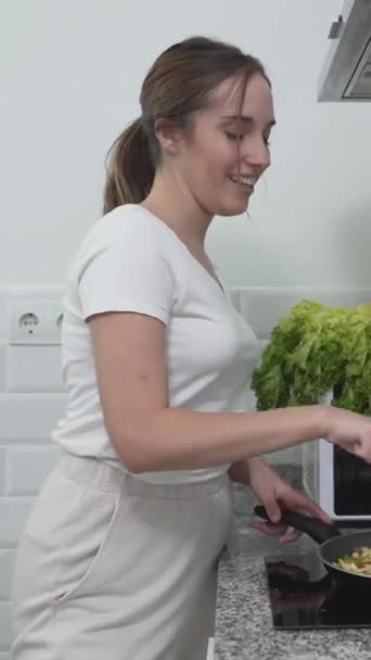 Onnellinen tyttö laulaa keittäessään kasvisruokaa keittiössä. Keskikokoinen laukaus - Pystysuora - Materiaali, video