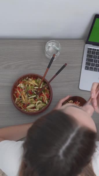 Vista superior de una mujer comiendo almuerzo en el escritorio en frente de la computadora portátil con pantalla verde. gastos generales - Vertical - Metraje, vídeo