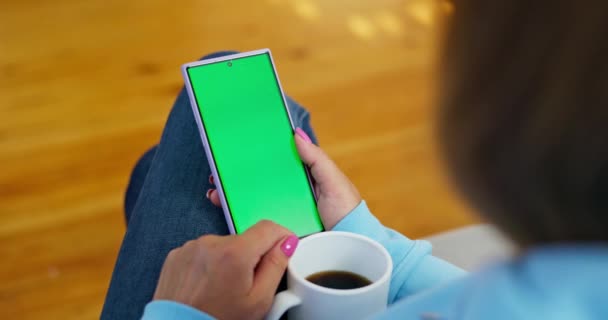 Blick über die Schulter einer Frau, die ein Telefon mit grünem Bildschirm benutzt und eine Kaffeetasse in der Hand hält. Hochwertiges 4k Filmmaterial - Filmmaterial, Video