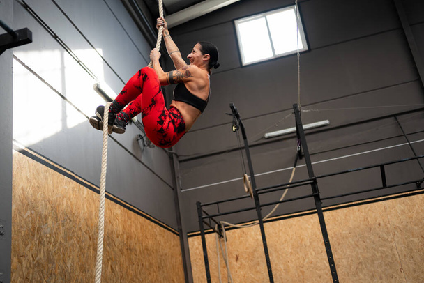 Low angle view photo with copy space of a fit mature woman climbing a rope in a cross training gym - Photo, Image
