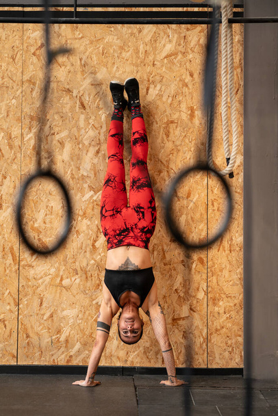 Vertical photo of a sportive mature woman performing handstand exercise in the gym - Photo, Image