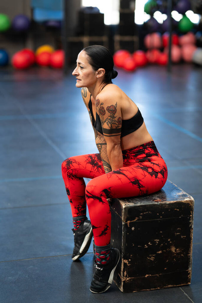 Vertical side view photo of a mature athlete resting sitting on a box in a gym - Photo, Image