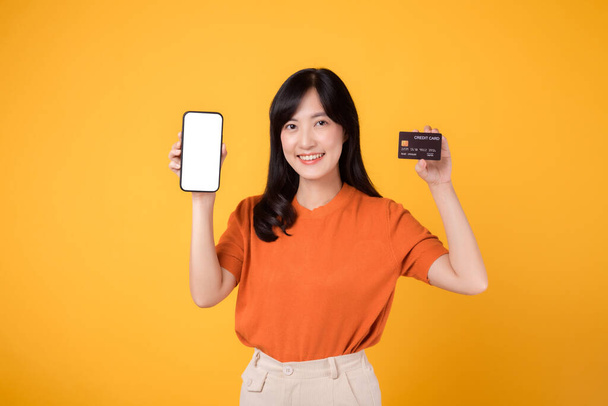 Nadšený asijské ženy 30s, prezentující smartphone a kreditní kartu na žlutém pozadí. Pohodlné nakupování online plateb. - Fotografie, Obrázek