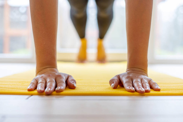 Hands pressed flat on yellow yoga mat, workout session indoors. - Photo, Image