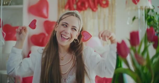 Χαρούμενη νεαρή γυναίκα που κρατά καραμέλες σε σχήμα καρδιάς κατά τη διάρκεια της ημέρας Galentines - Πλάνα, βίντεο