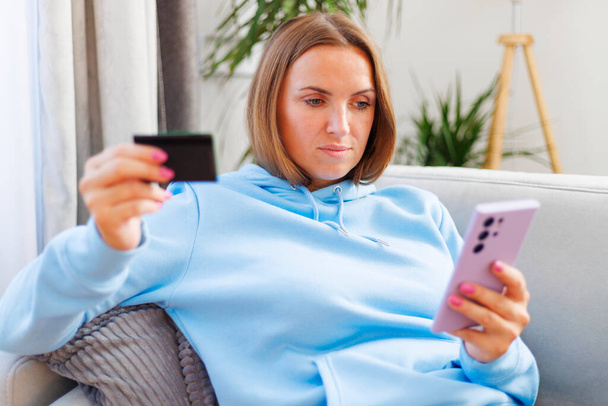 Nő kék kapucnis segítségével okostelefon és hitelkártya az online vásárlás - Fotó, kép