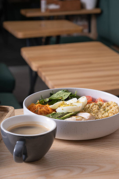 Miska kuskusu, mięsa, jajek, awokado i warzyw oraz filiżanka kawy na stoliku kawiarni - Zdjęcie, obraz