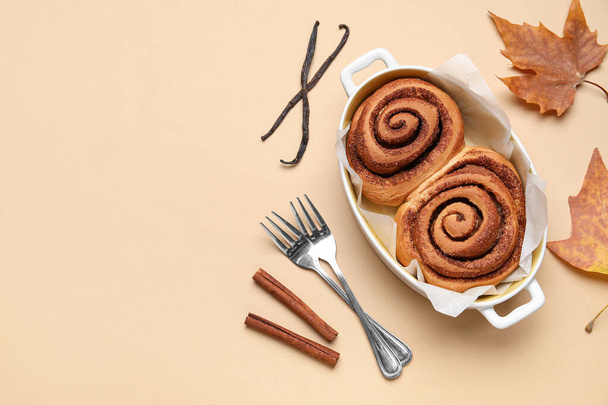 Baking dish of tasty cinnamon rolls and autumn leaves on beige background - Photo, Image