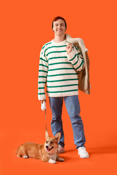 Kızıl saçlı genç adam turuncu arka planda şirin Corgi köpeğiyle yürüyüşe çıkıyor. - Fotoğraf, Görsel