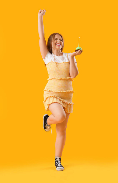 Красива молода щаслива жінка з кексом на жовтому фоні - Фото, зображення