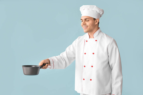 Przystojny szczęśliwy szef kuchni z garnkiem na niebieskim tle - Zdjęcie, obraz