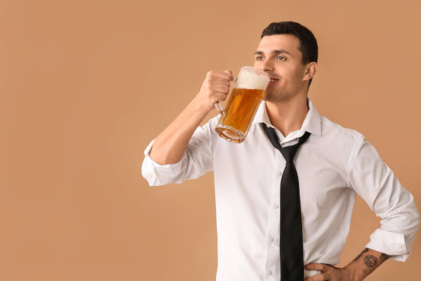 Komea nuori onnellinen mies juo olutta ruskealla taustalla - Valokuva, kuva