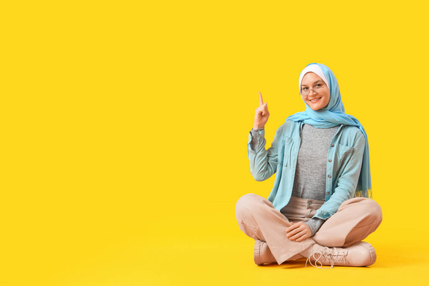 Gyönyörű fiatal boldog muszlim nő hidzsáb elegáns napszemüveg mutat valamit sárga alapon - Fotó, kép