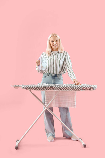 Ευτυχισμένη ώριμη γυναίκα σιδέρωμα ρούχα σε ροζ φόντο - Φωτογραφία, εικόνα