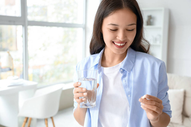 自宅で水と錠剤のガラスを持つ若いアジアの女性 - 写真・画像