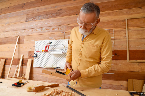 Carpinteiro maduro medindo prancha de madeira na loja - Foto, Imagem