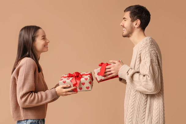 Красива молода пара з подарунковими коробками на коричневому тлі. Святкування Дня святого Валентина - Фото, зображення