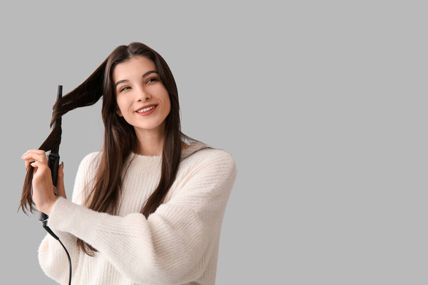 Belle jeune femme heureuse frisant ses cheveux sur fond gris - Photo, image