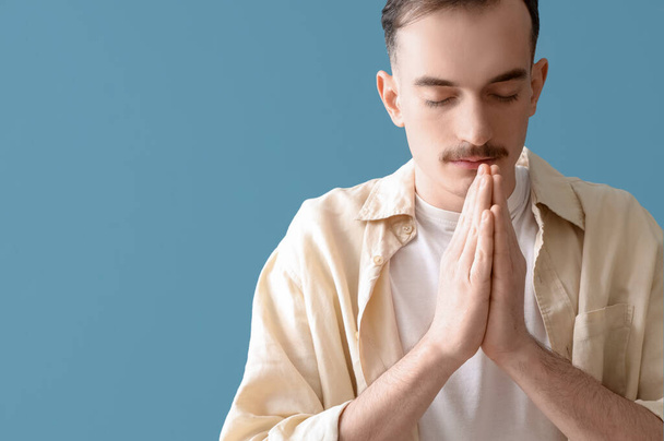 Junger Mann betet auf blauem Hintergrund, Nahaufnahme - Foto, Bild