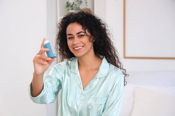 Mujer joven afroamericana con inhalador de asma en el dormitorio - Foto, imagen