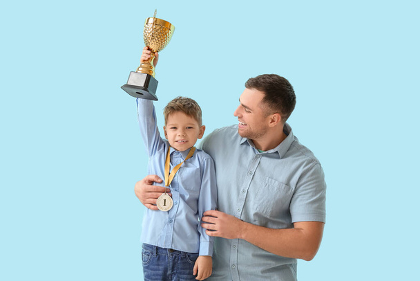 Счастливый отец и его маленький сын с медалью, держа золотую чашку на синем фоне - Фото, изображение
