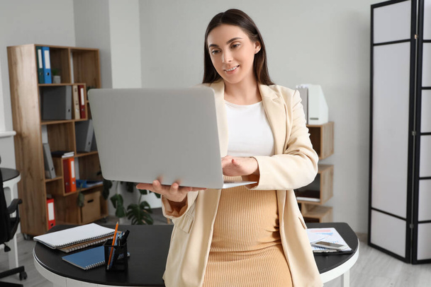 Беременная деловая женщина с ноутбуком, работающая в офисе - Фото, изображение