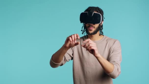 entusiasta da tecnologia vestindo óculos de realidade virtual, fazendo gestos furto. BIPOC homem usando alta tecnologia futurista óculos VR modernos, fazendo tátil toque gestual, fundo estúdio azul - Filmagem, Vídeo